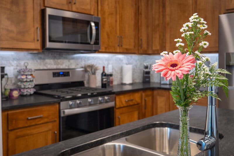 kitchen with range, microwave above range, upper cabinets and black countertops. kitchen island with sink and pink flower in fore ground.