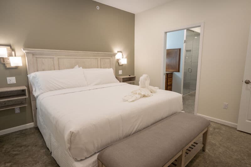 king size bed with white linens. bedside tables with sconces on wall above. bench at foot of bed