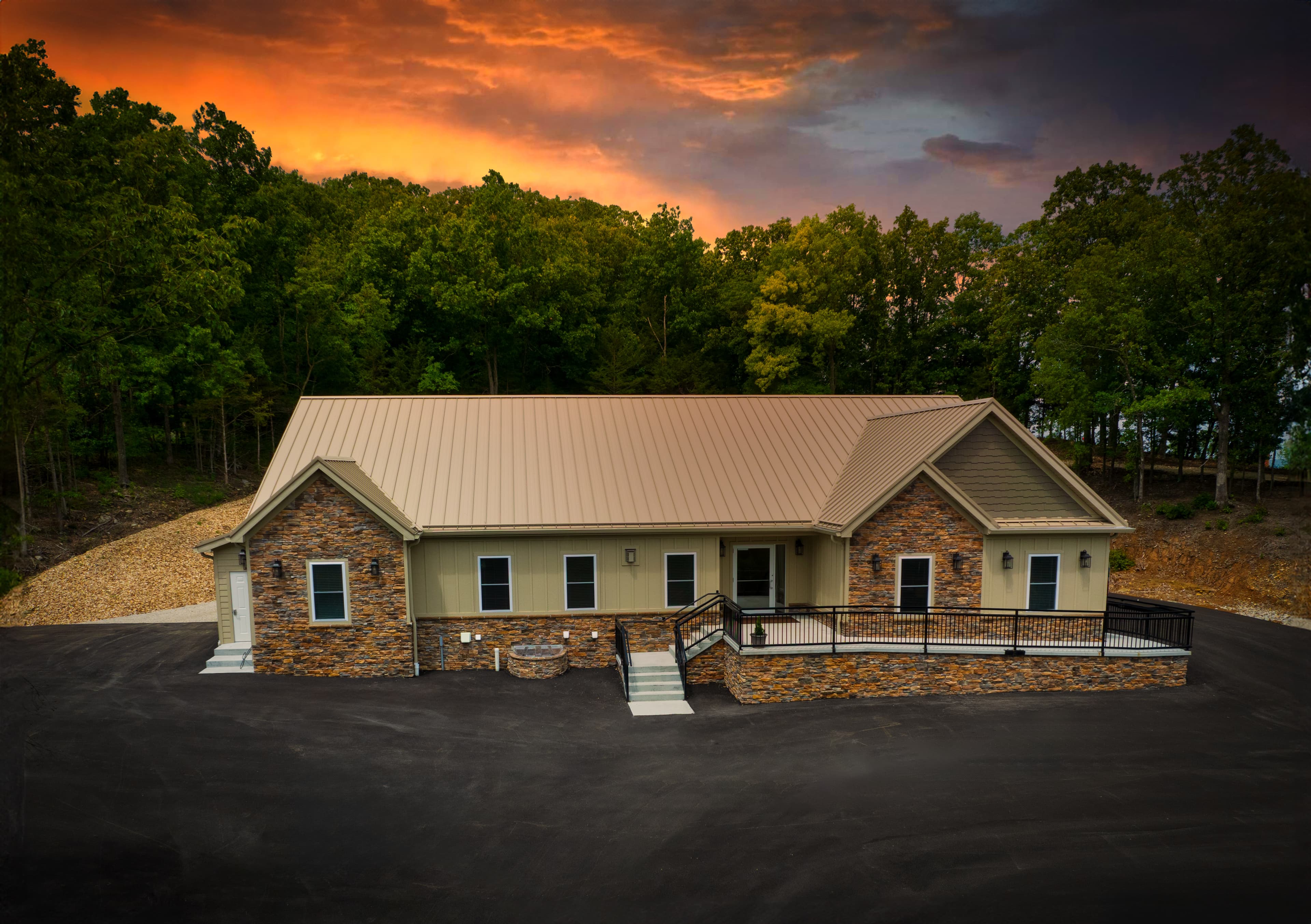 Exterior long view of a single-story building, brick and siding with ramp and stares to main entrance, parking lot in front and trees behind building. orange and gray sunset with some clouds in the sky