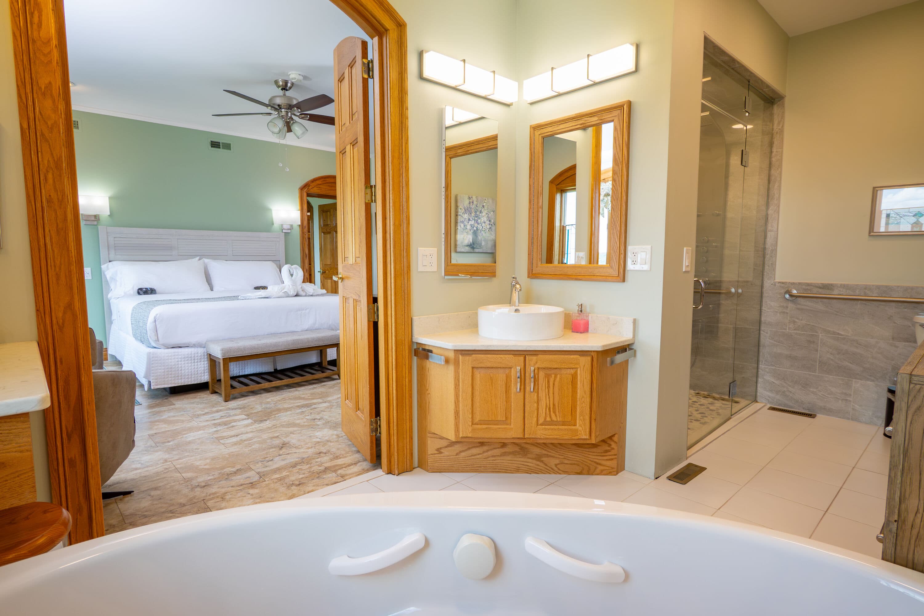 view from jetted tub looking out at sink and shower with king size bed in background outside of bathroom