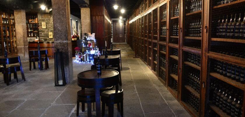 A dimly lit wine cellar featuring wooden shelves filled with wine bottles and a small seating area.