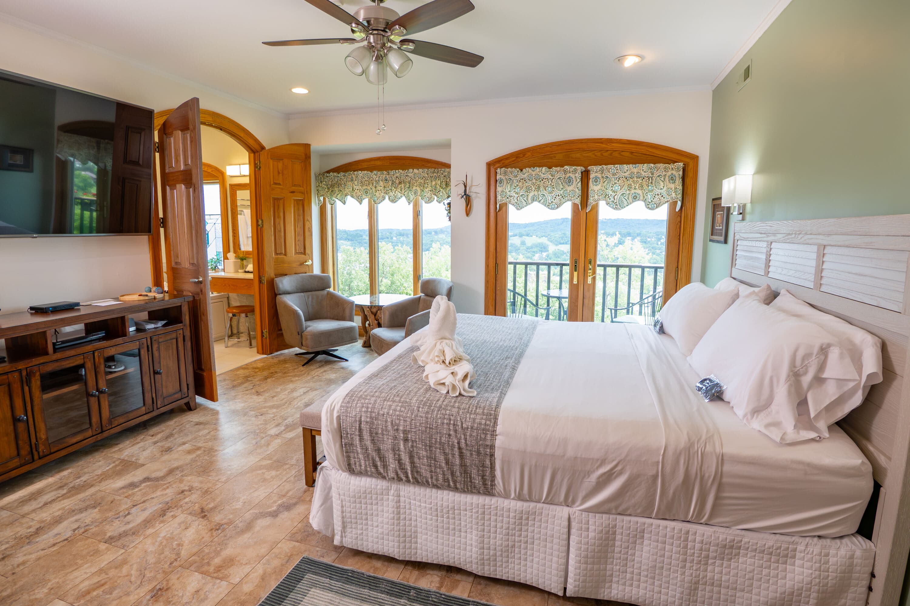 bedroom with king size bed and chairs a flat screen TV and large windows adn french doors with view outside