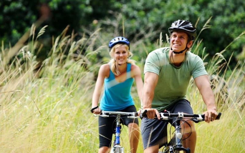 A man and woman happily ride bicycles through tall grass.