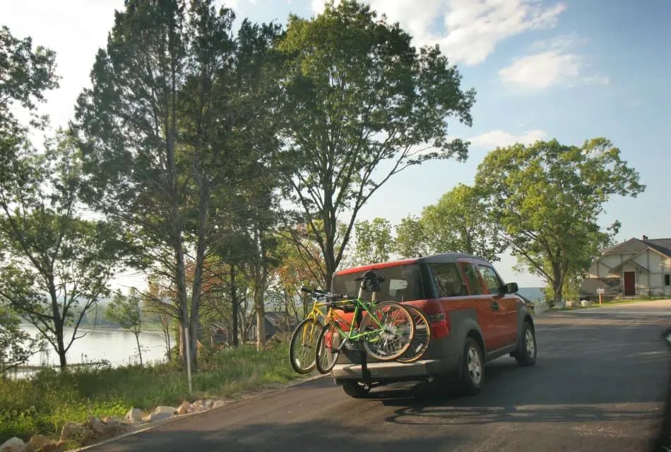 Vehicle with bikes attached driving on paved road with trees and river in the background