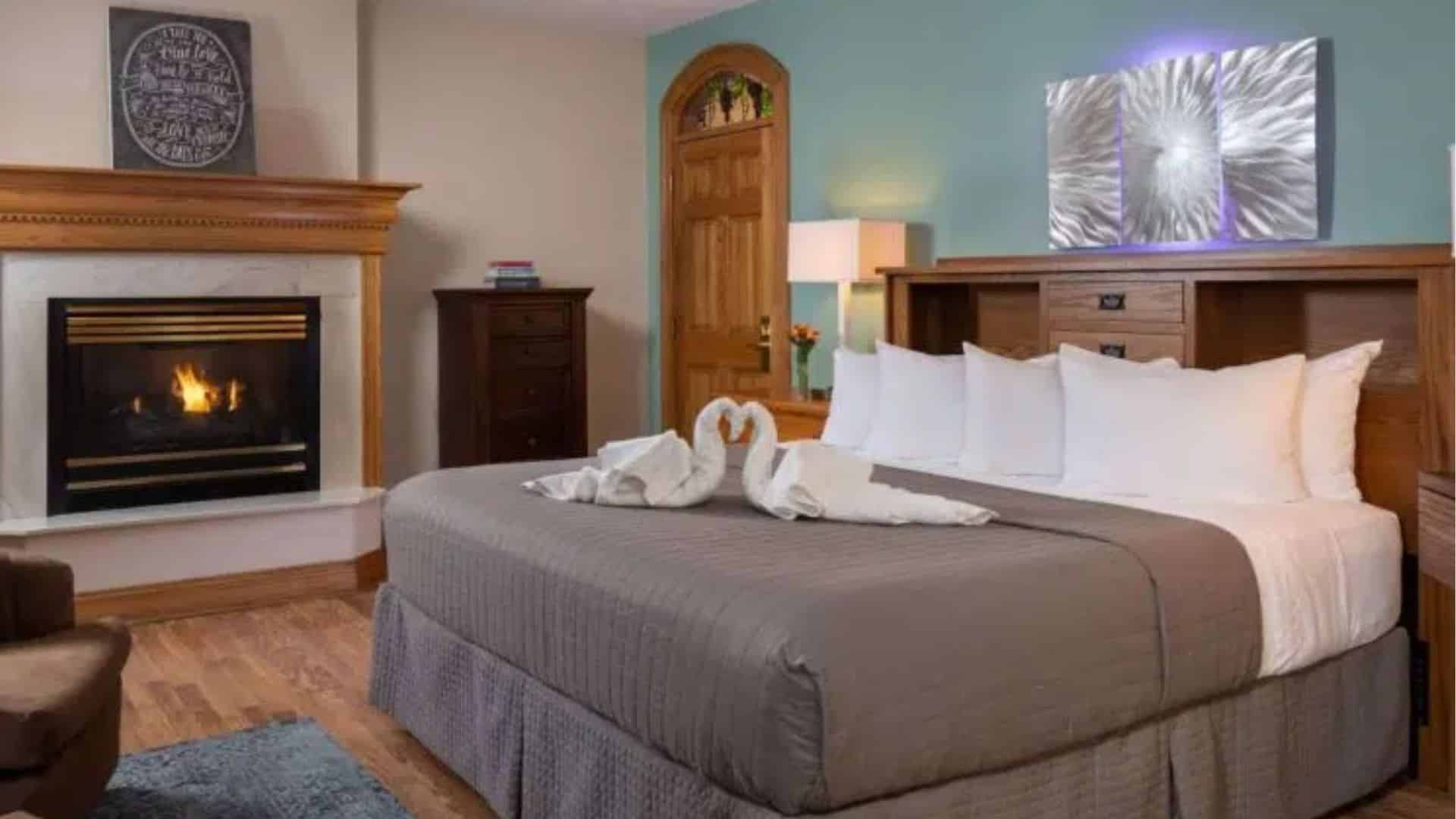A cozy hotel room featuring a king-sized bed, fireplace, and decorative towels shaped like swans.