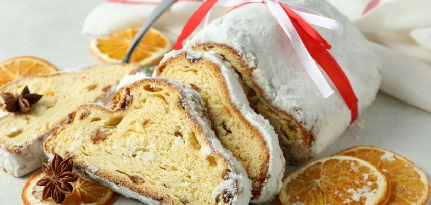 A sliced loaf of stollen bread, decorated with powdered sugar and served with orange slices and star anise.