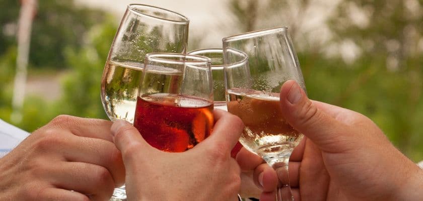 Four glasses are raised in a toast outdoors.