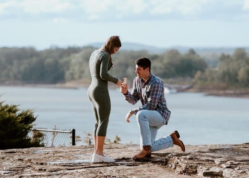 A man is kneeling and proposing to a woman in a scenic outdoor setting. A man is kneeling and proposing to a woman in a scenic outdoor setting.