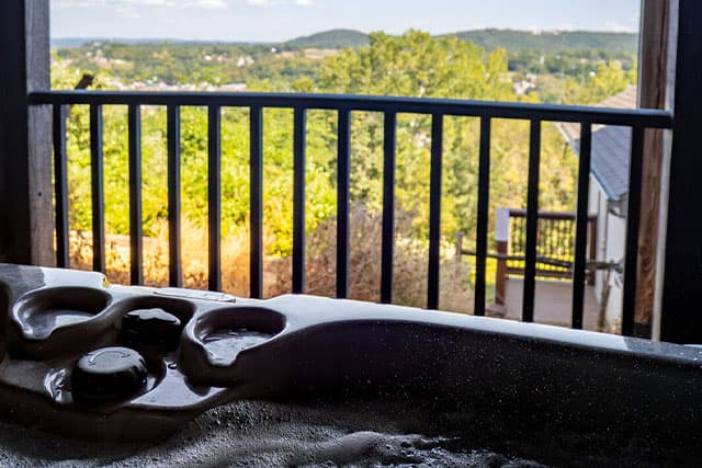 View of a bubbling hot tub with a scenic landscape and railing in the background.