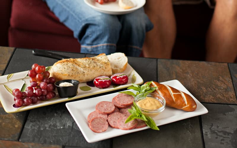 A platter of grapes, bread, and cheese alongside a selection of meats and pretzels with mustard.