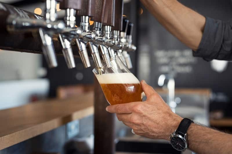 A person pours a pint of beer from a tap at a bar.