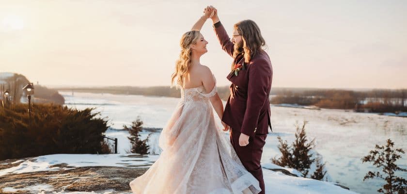 A couple dances together on a rocky outcrop with a scenic river view during sunset.