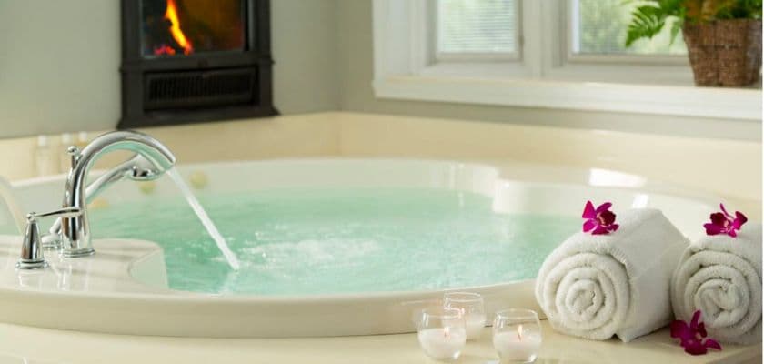 A luxurious spa jacuzzi with flowing water, surrounded by rolled towels and candles.
