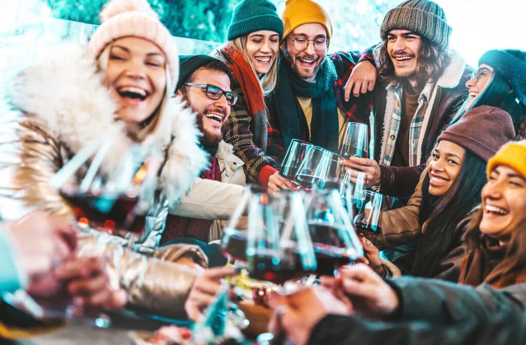 A diverse group of friends joyfully clinks glasses of red wine while laughing together in a festive setting.