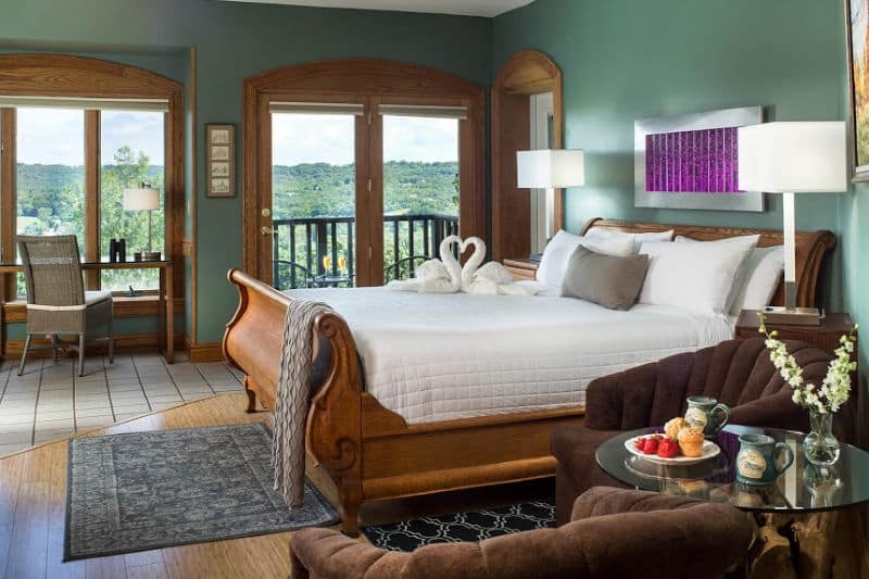 A cozy bedroom featuring a wooden sleigh bed, two armchairs, and large windows with a scenic view.