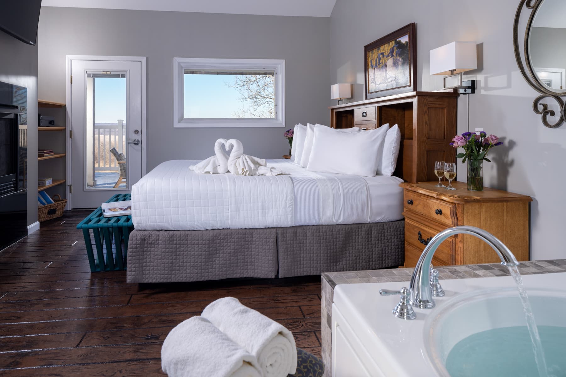 A cozy hotel room featuring a neatly made bed, a jacuzzi, and a view through large windows.