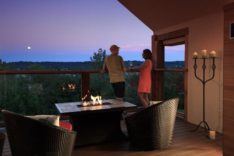 A couple enjoys a sunset view from a balcony with a firepit and candlelit ambiance.