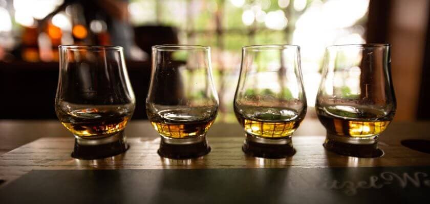 Four whiskey tasting glasses with varying levels of amber liquid, arranged on a wooden surface.