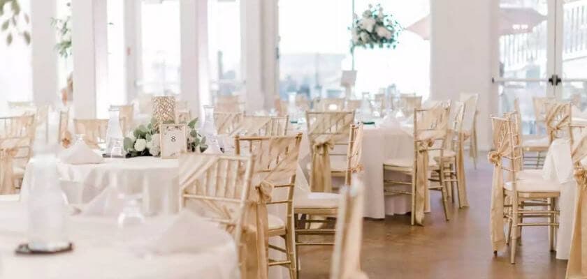 A beautifully arranged banquet hall with round tables and golden chairs, ready for an event.