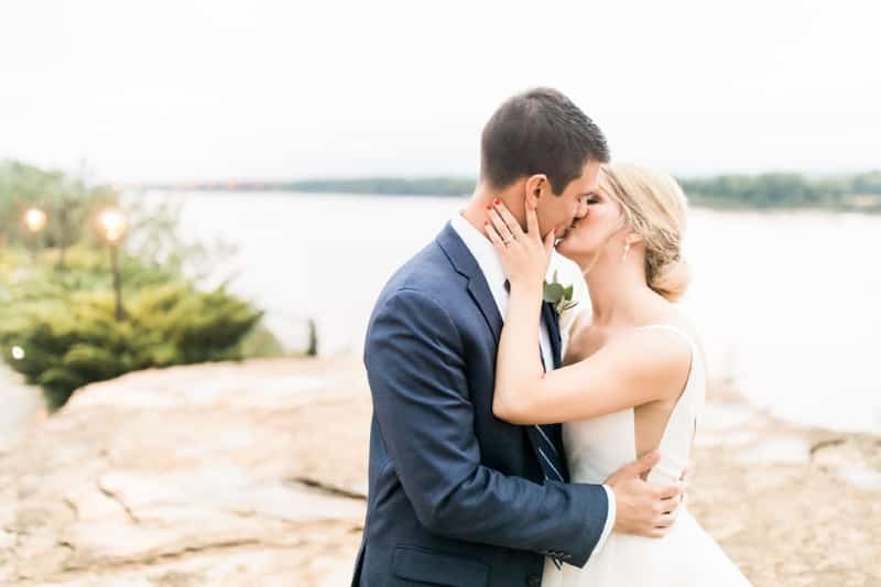 A bride and groom share a kiss on a rocky outcrop with a scenic background.