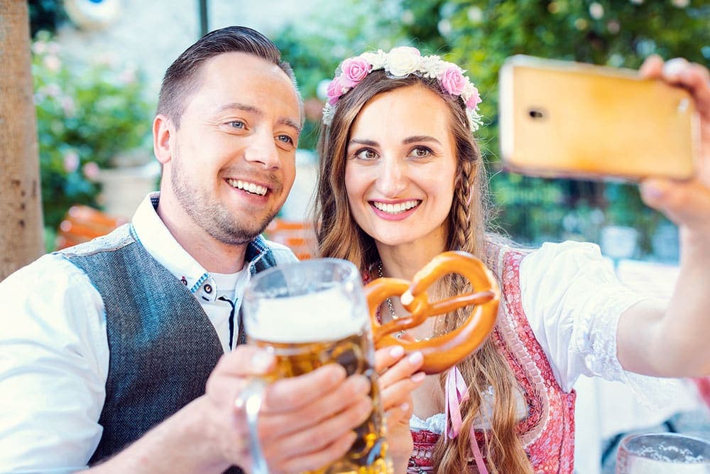 A smiling couple takes a selfie while holding a large beer and a pretzel.