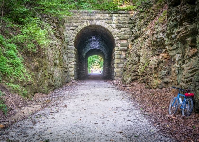 A gravel path leading through a stone archway tunnel, with a blue bicycle parked nearby.