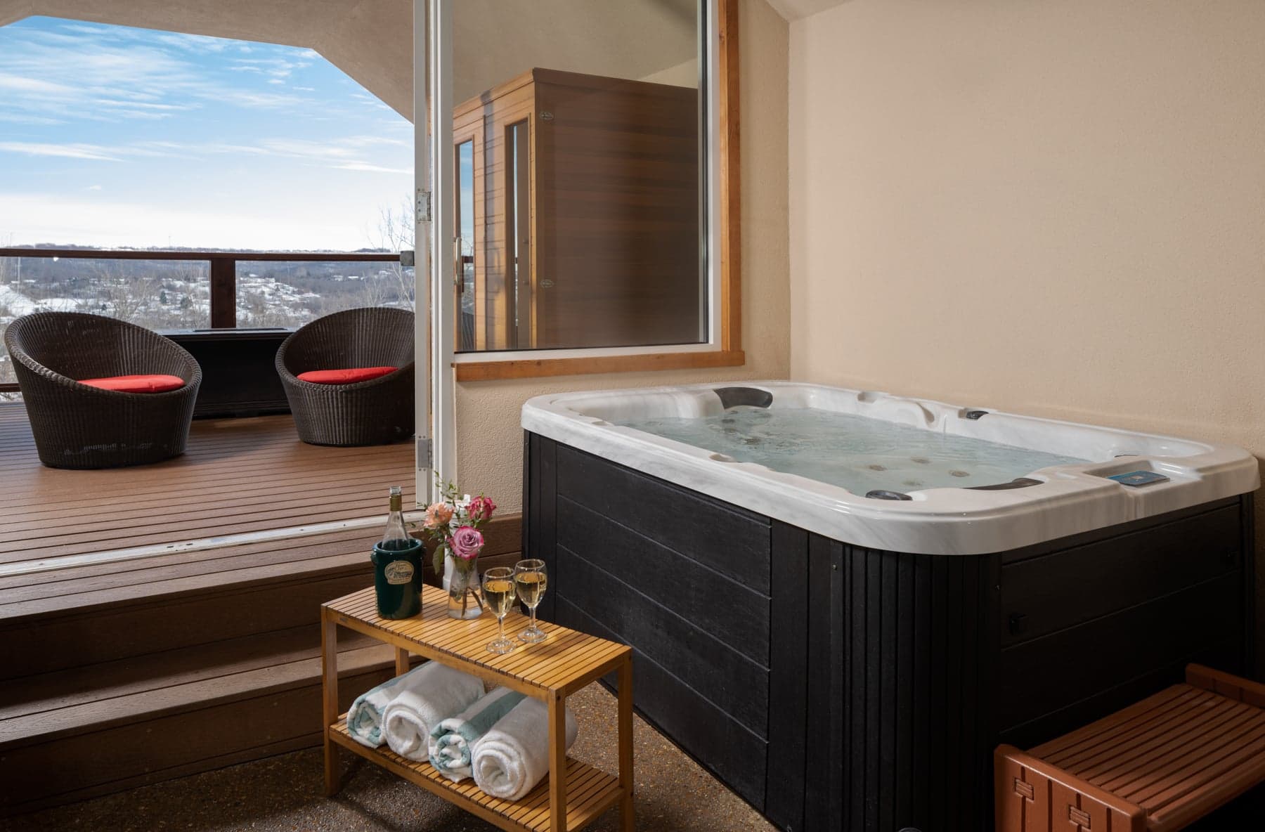 A cozy balcony features a hot tub, with two chairs, a small table, and a scenic view.