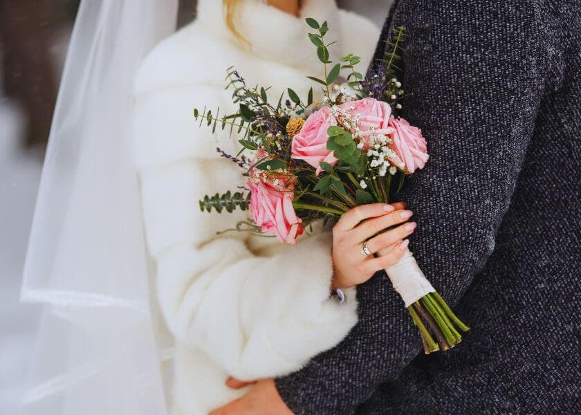 A bride in a white coat holds a bouquet of pink roses while embracing her partner. A bride in a white coat holds a bouquet of pink roses while embracing her partner.