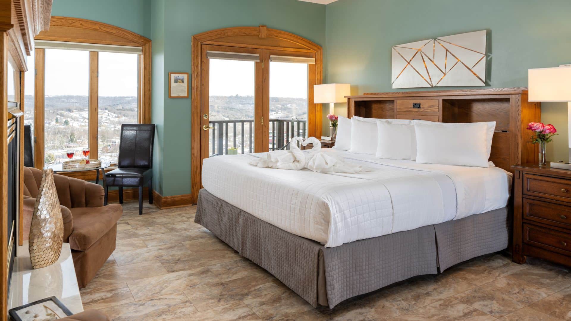 A cozy hotel room featuring a king-sized bed, a pair of armchairs, and large windows with scenic views.