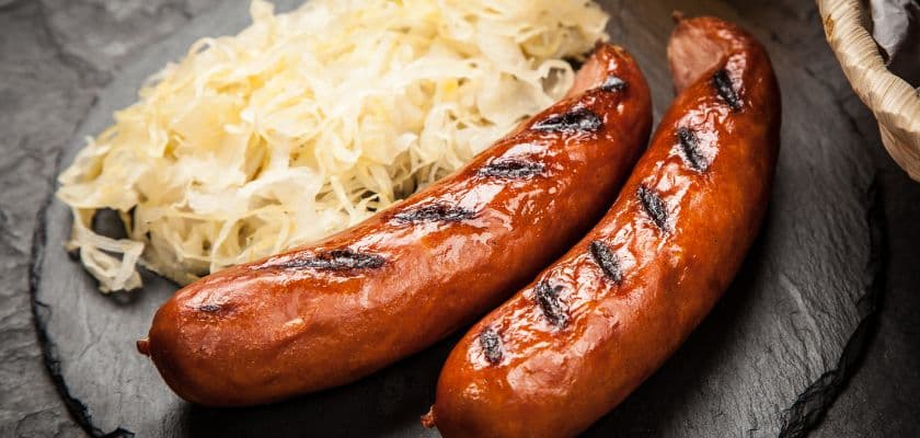 Two grilled sausages served with shredded sauerkraut on a black plate.