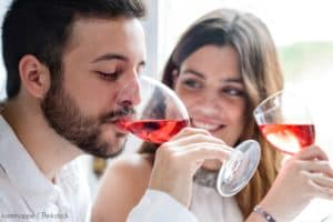 A man and woman clink glasses while smiling and enjoying drinks at a table.