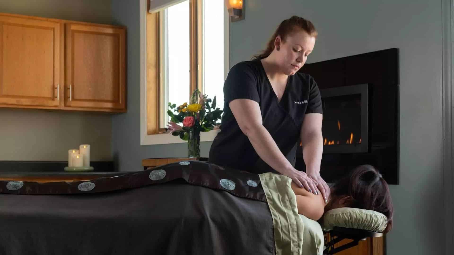 A massage therapist provides a massage to a client in a cozy, well-lit room.