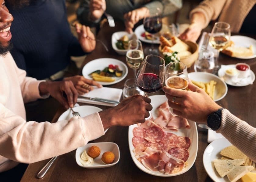 A group of friends is seated at a table, surrounded by food, and toasting each other with wine. A group of friends is seated at a table, surrounded by food, and toasting each other with wine.