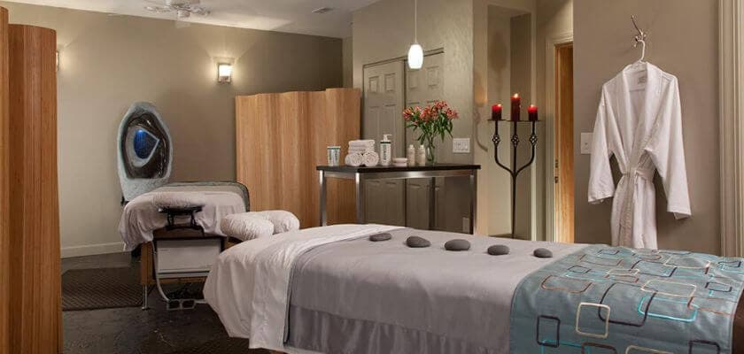 Spa room and bed with hot stones, candelabra, robe hanging on the wall, and lotions and oils on a table at Hermann Hill.