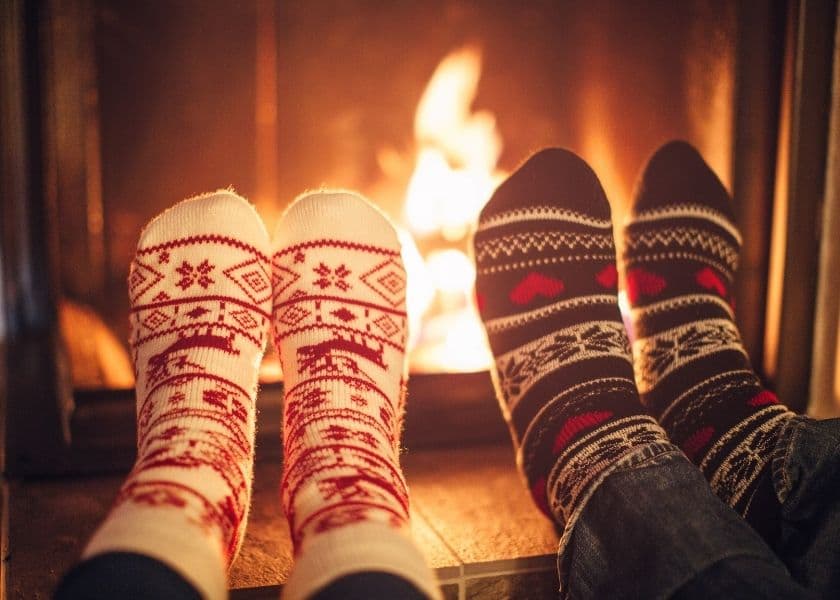closeup of two pairs of feet wearing sweater socks propped up by a lit fireplace closeup of two pairs of feet wearing sweater socks propped up by a lit fireplace