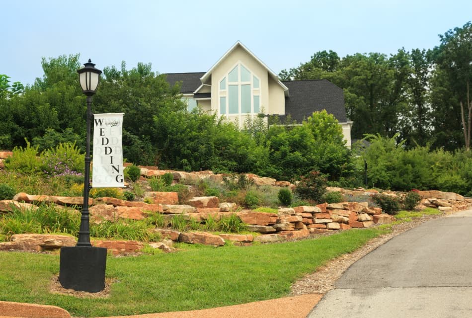 Exterior view of one of the buildings on the property surrounded by a garden with large stones and green vegetation and a lamp post with a wedding sign
