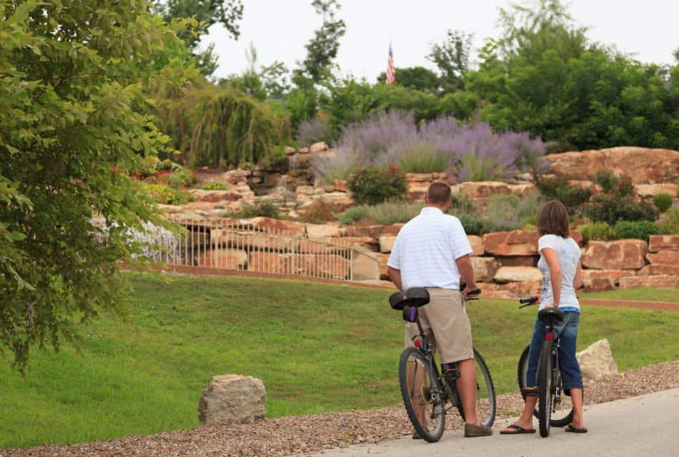 Man and woman with bikes looking at garden full of large stones, purple grasses, and pink flowering bushes