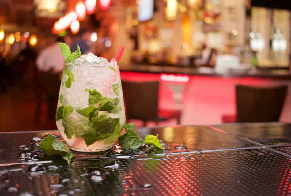 Close up view of a mojito drink in a medium glass with pink straw and extra mint leaves on the table