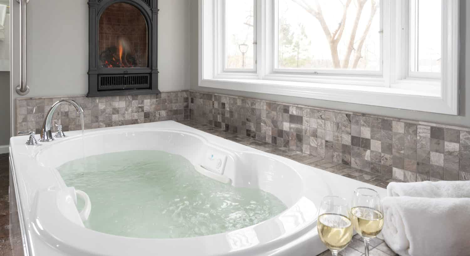 Large jetted tub filled with water and surrounded by tile in shades of gray