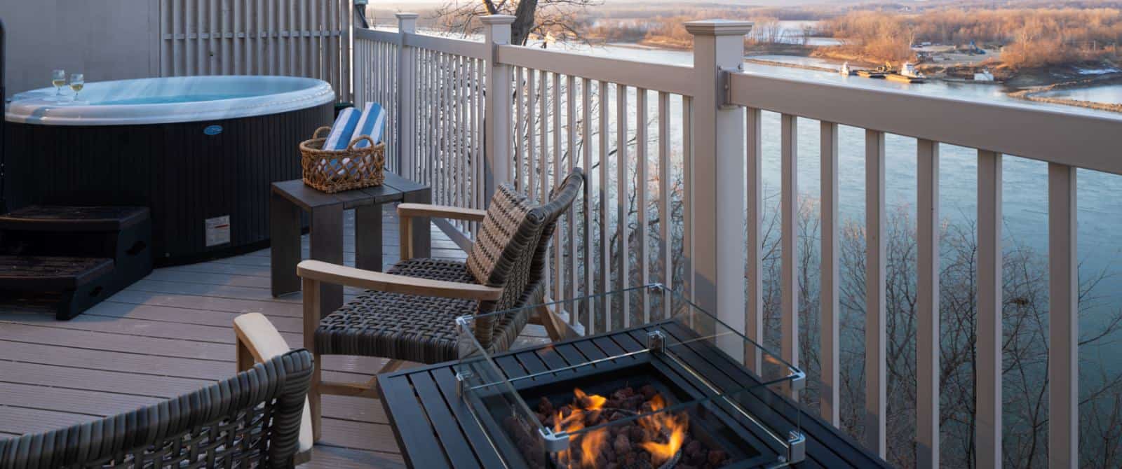 Deck with lighted table fire pit, wicker patio chairs, small jetted tub, and view of river in the background