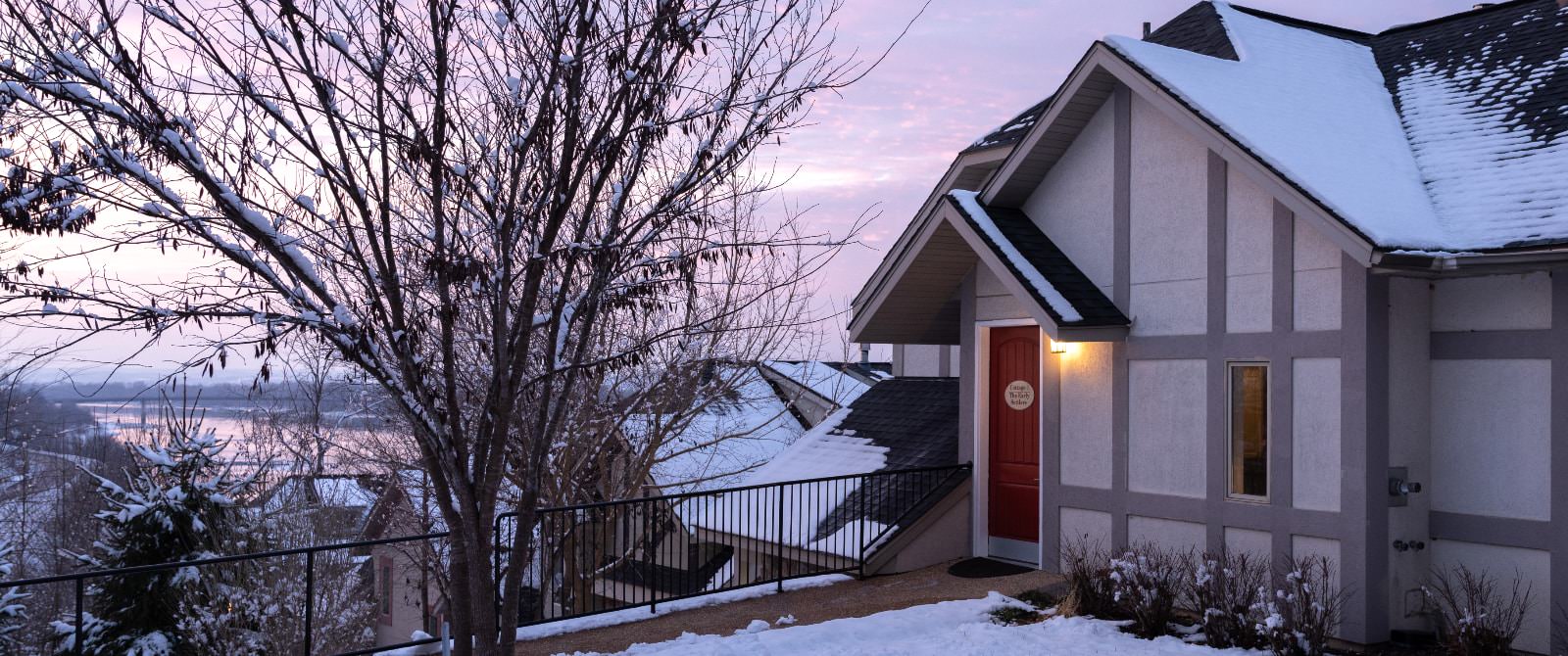 Exterior view of one of the cottages with pathway leading up to red door covered by snow at dusk