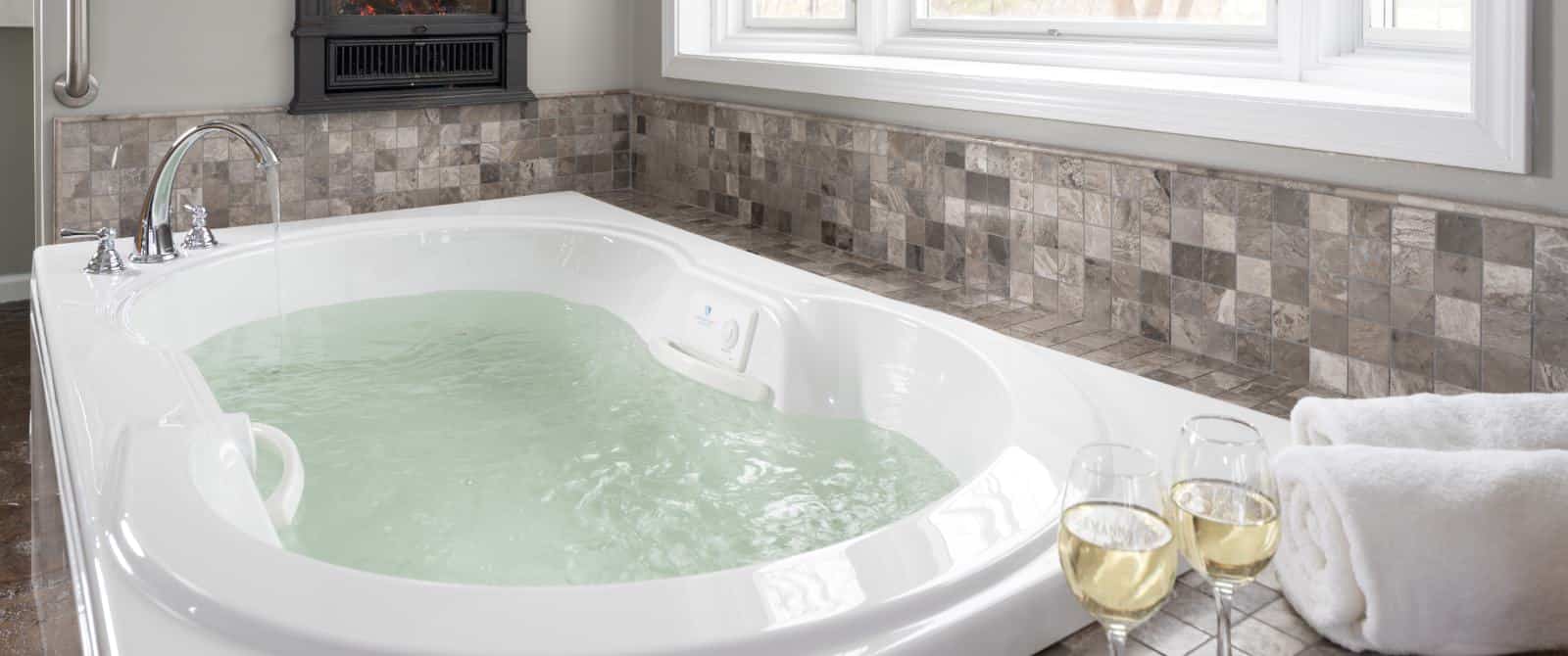 Large jetted tub filled with water and surrounded by tile in shades of gray