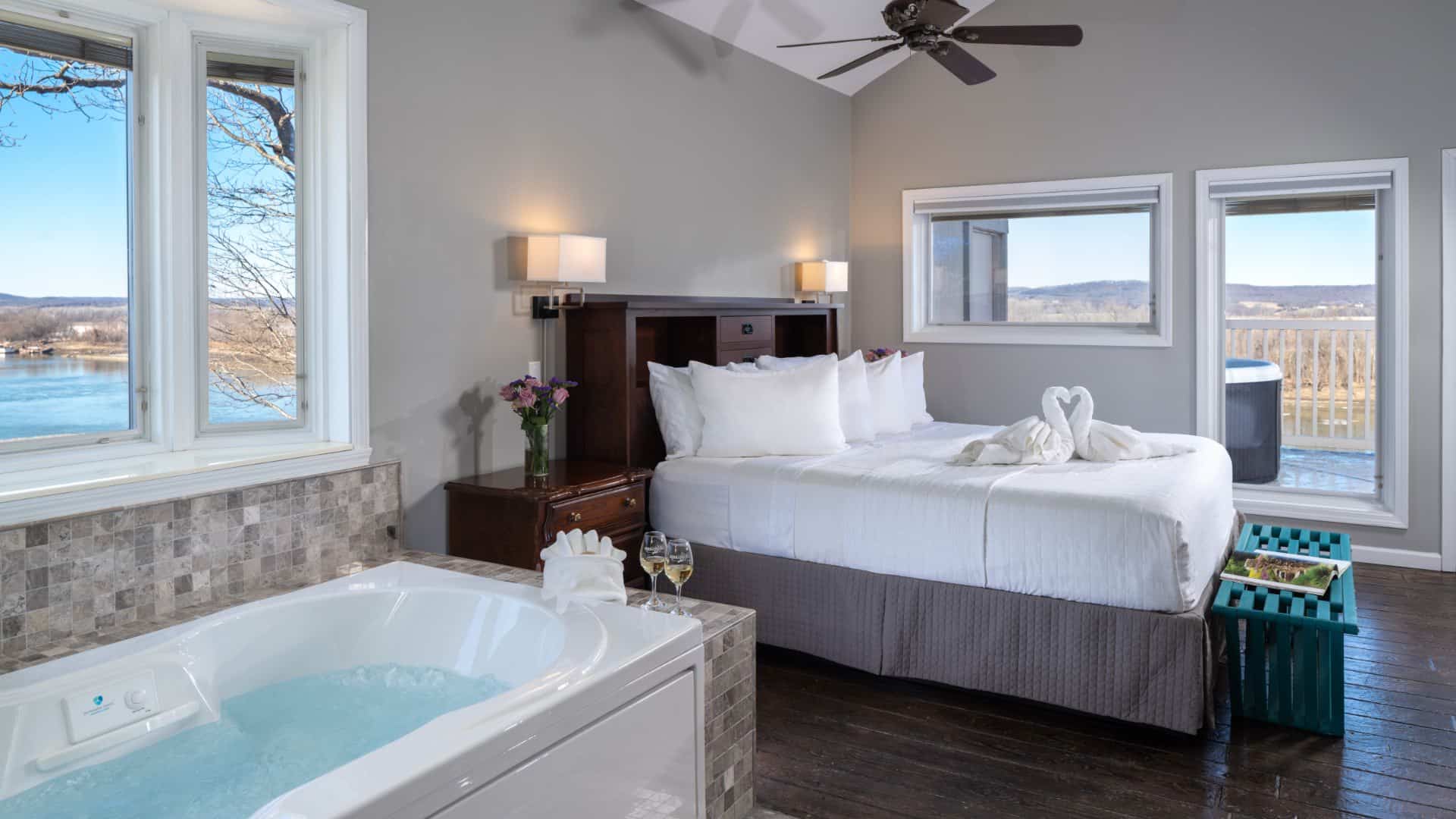Large bedroom suite with light gray walls, tiled flooring, wooden headboard, white bedding, gray comforter, and jetted tub