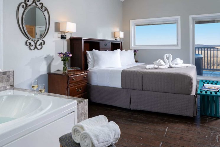 Large bedroom suite with light gray walls, tiled flooring, wooden headboard, white bedding, gray comforter, and jetted tub