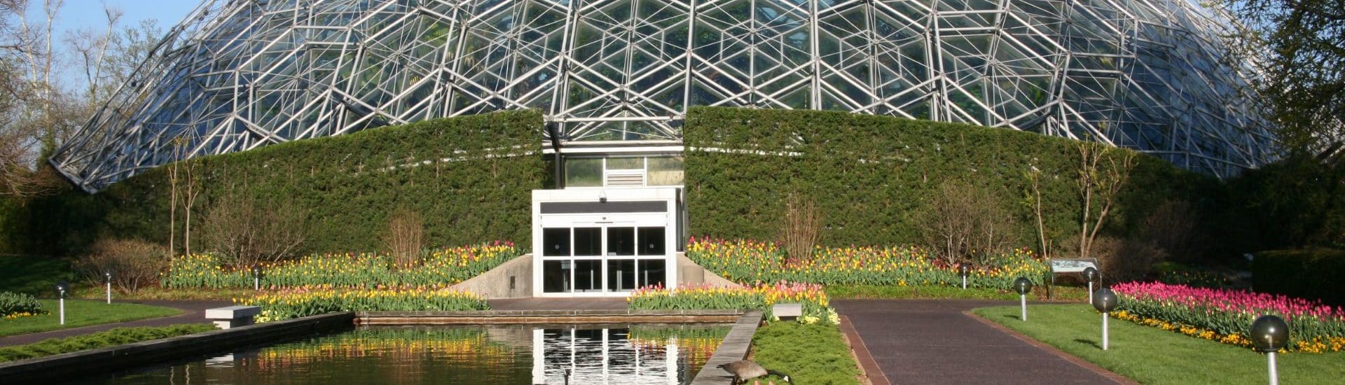 Large, white Climatron Geodesic Dome Conservatory surrounded by plants, flowers and trees.