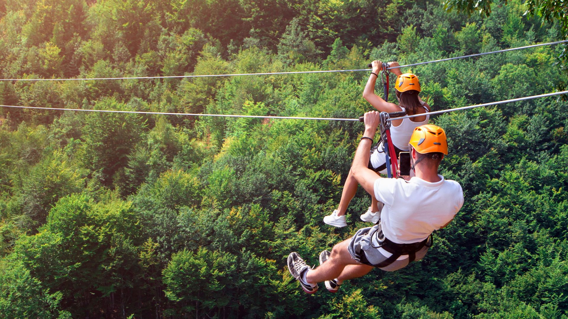 Couple ziplineing over the lush green tree tops