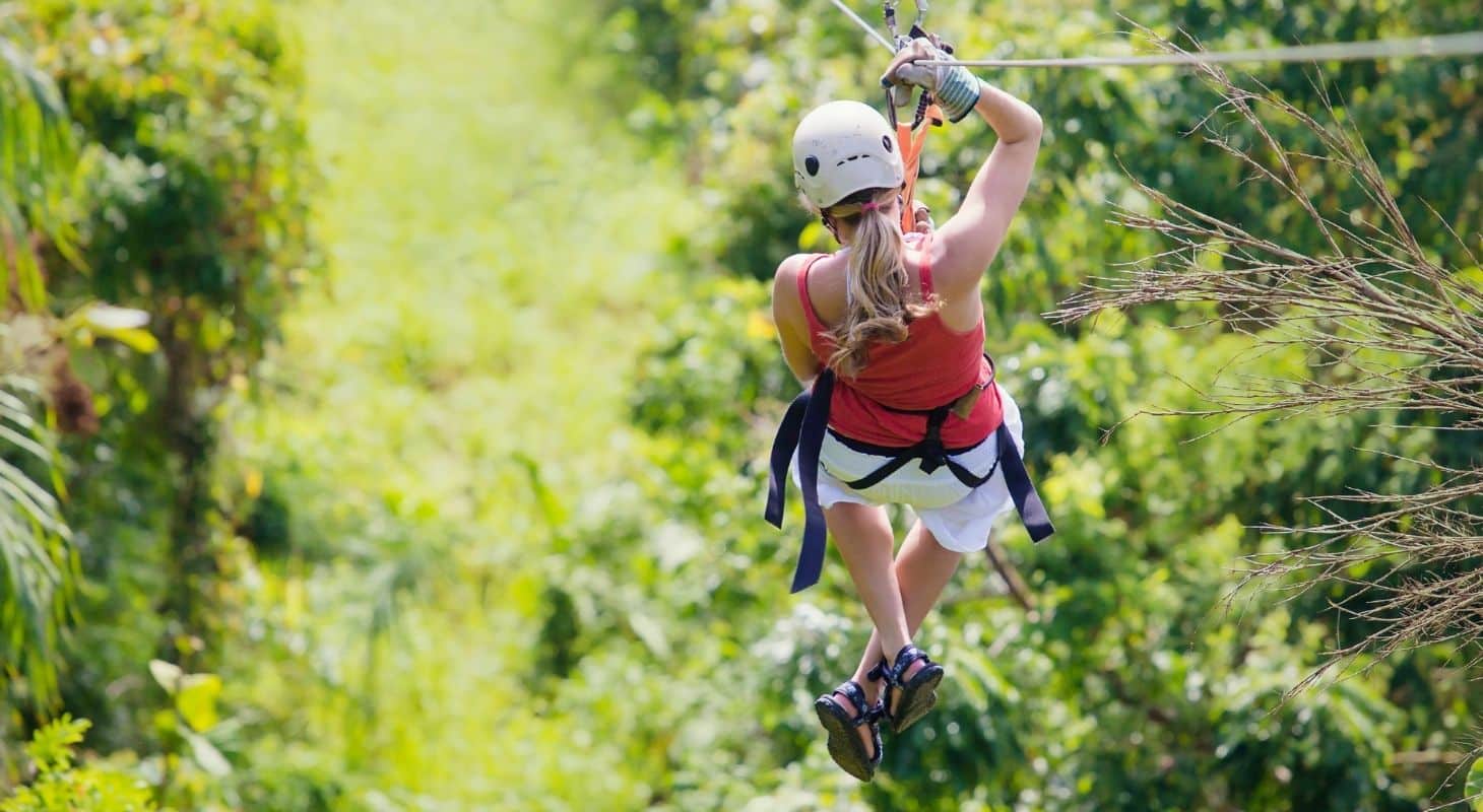 Woman ziplining through the trees surrounded by lush foliage