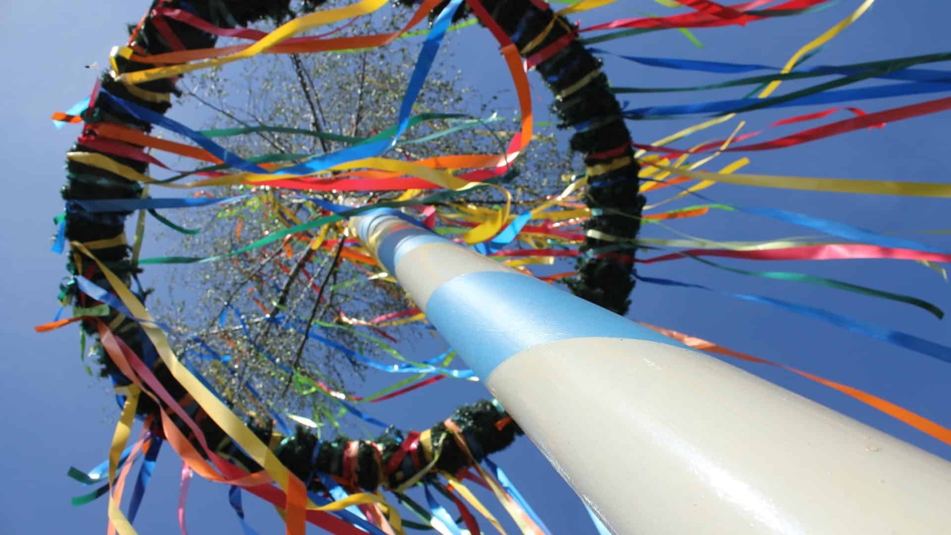 White maypole with colorful streamers hanging down against a blue sky