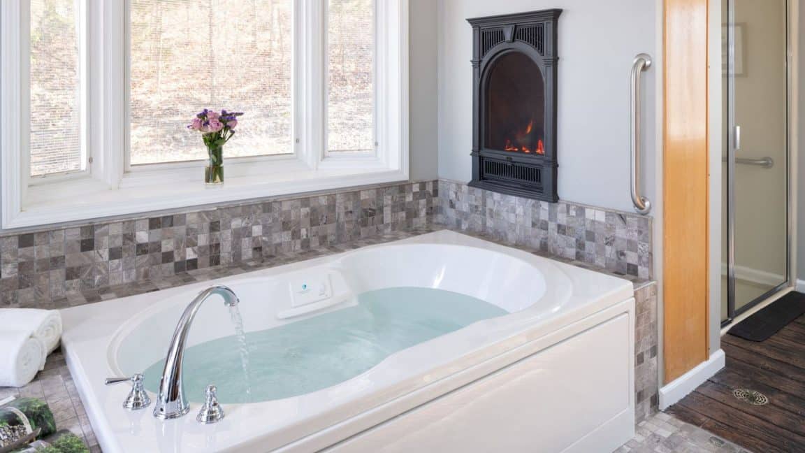 Jetted tub with tile surround, bay window and cozy fireplace