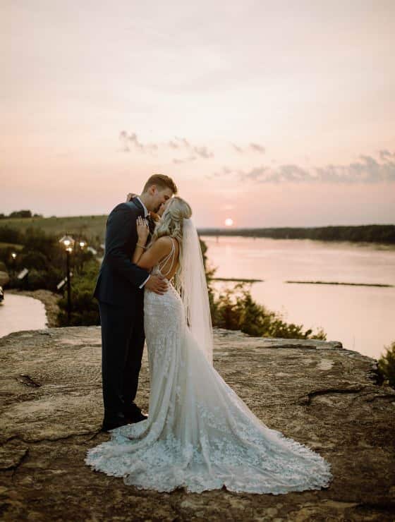 Bride and groom kissing while standing on large rock with river in the background